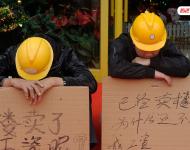 2012年12月25日，廣東中山，火炬開發(fā)區(qū)的多名建筑工人討要工作一年多的血汗錢一籌莫展，一些工人干脆將鋪蓋卷搬到了售樓部，并在門口搭起灶臺煮飯，希望以這種方式討回工錢。圖為在銷售中心門外，工人舉牌討薪。吳進/視覺中國